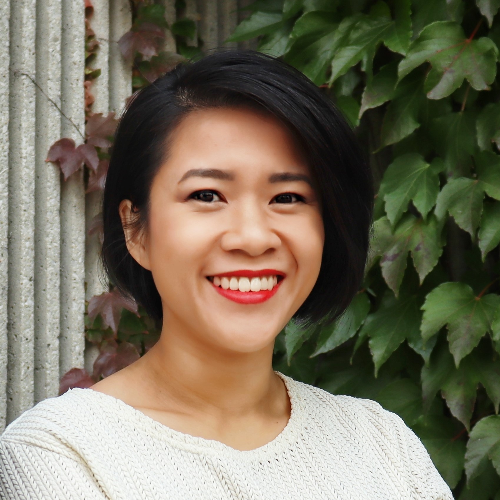 Bridjet, a medium-light skinned East Asian woman with short black hair, pictured from shoulders up, smiles at the camera.